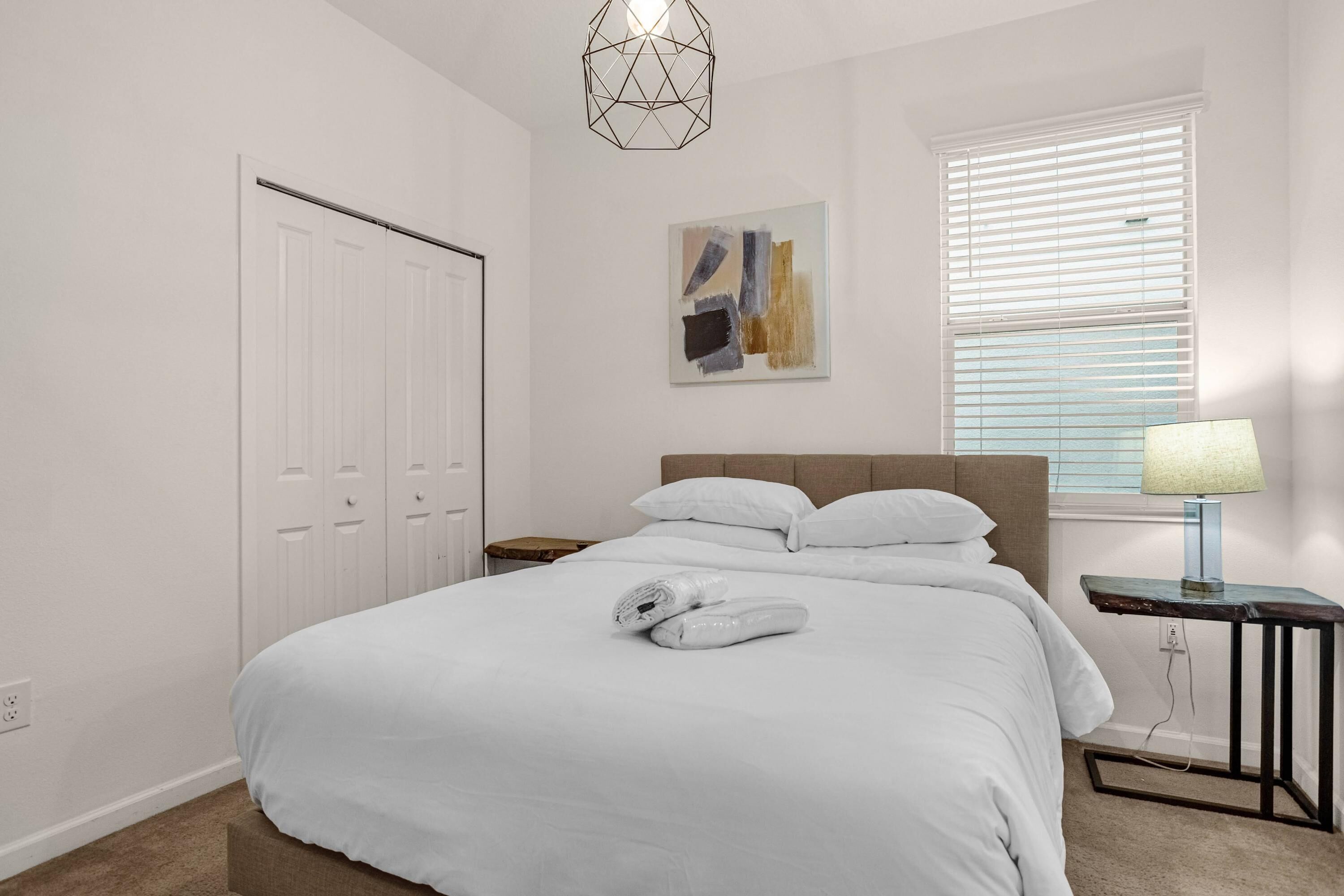A bedroom with a bed, a nightstand, a lamp, a painting, and a closet.