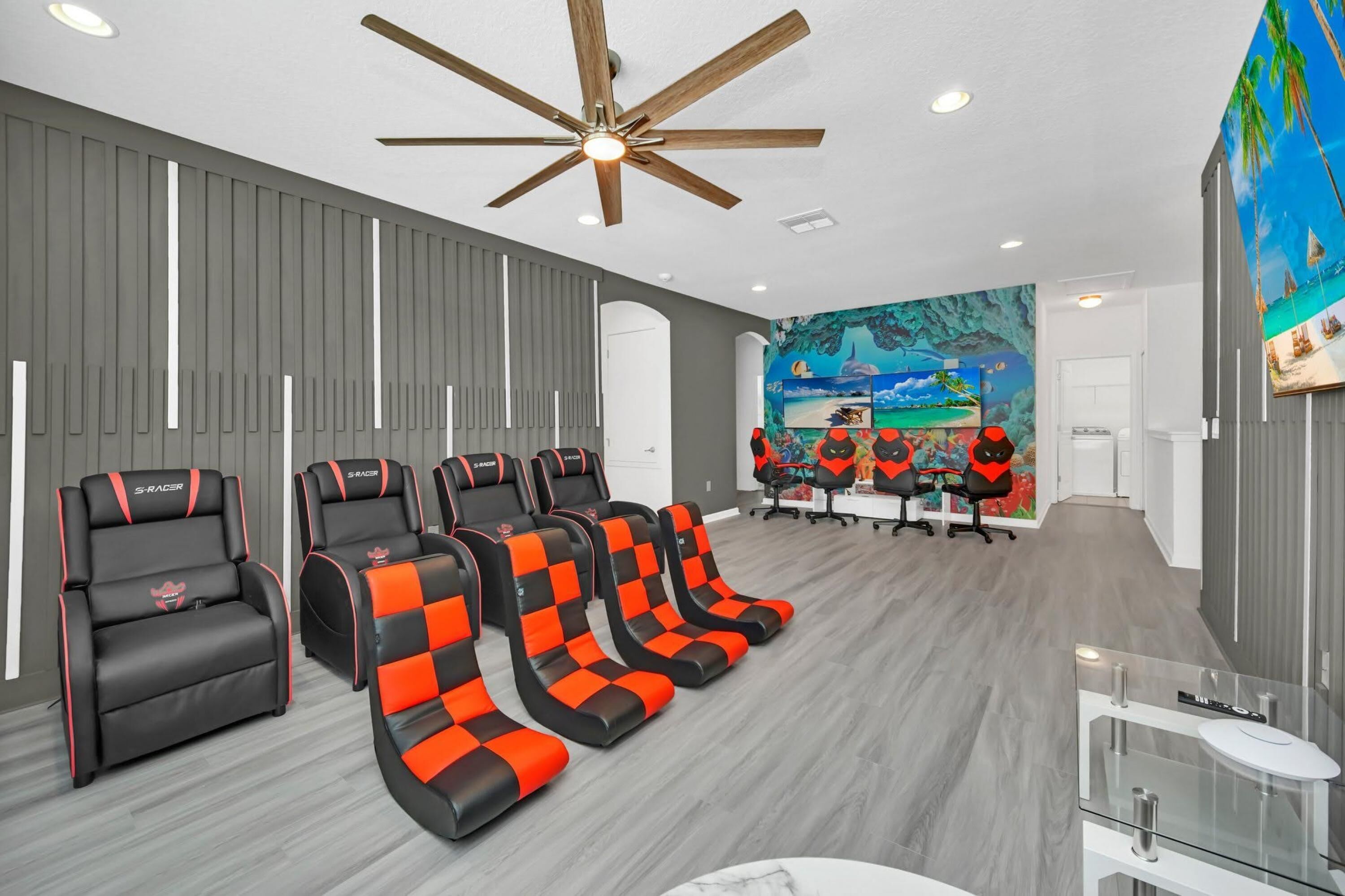 A room with a ceiling fan, a mural, and multiple racing chairs.