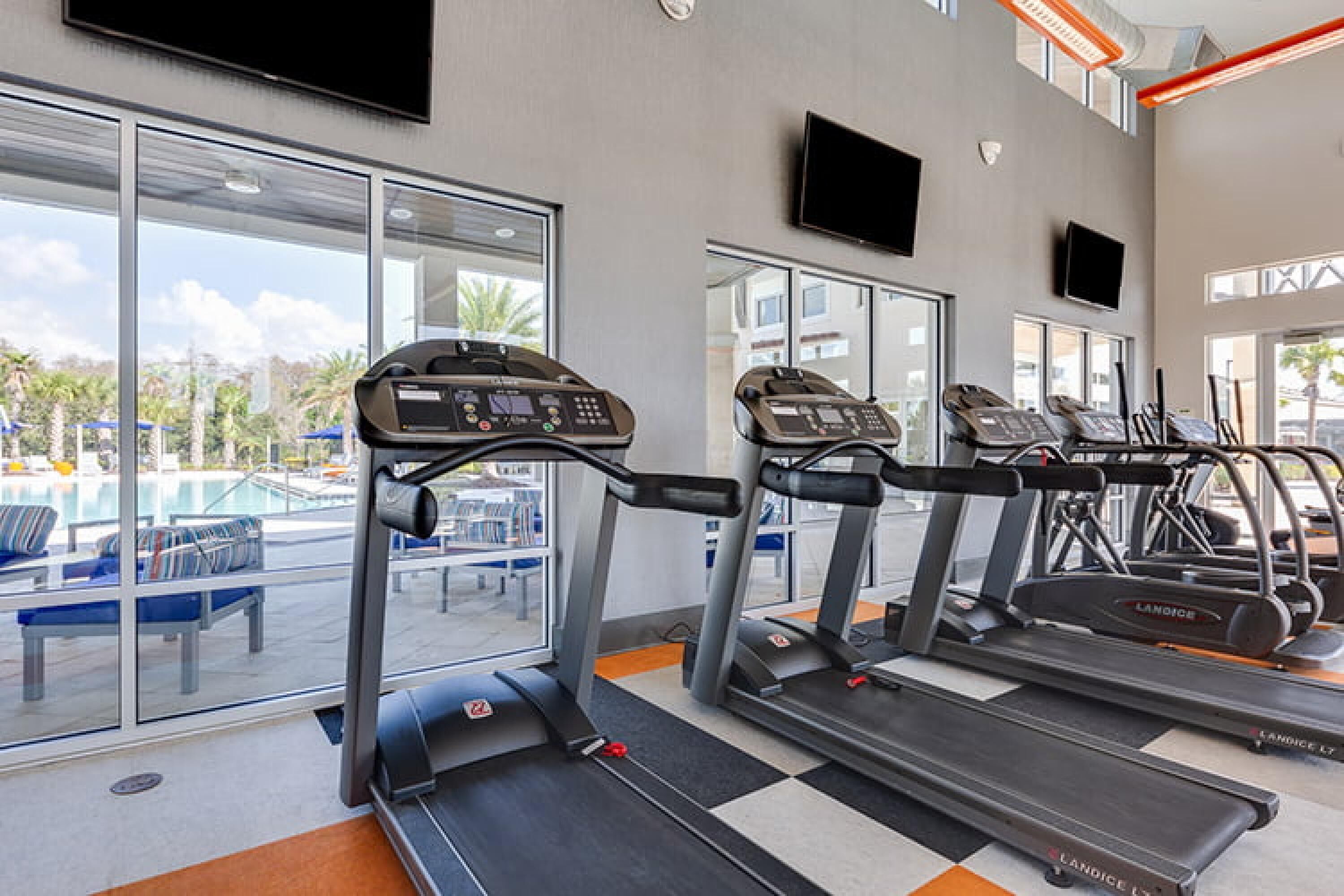 Une salle de sport équipée de tapis de course, d’appareils d’exercice et de grandes fenêtres donnant sur un espace piscine.