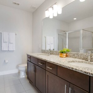 A modern bathroom with a granite countertop, dark wood cabinets, a large mirror, and a shower enclosure.