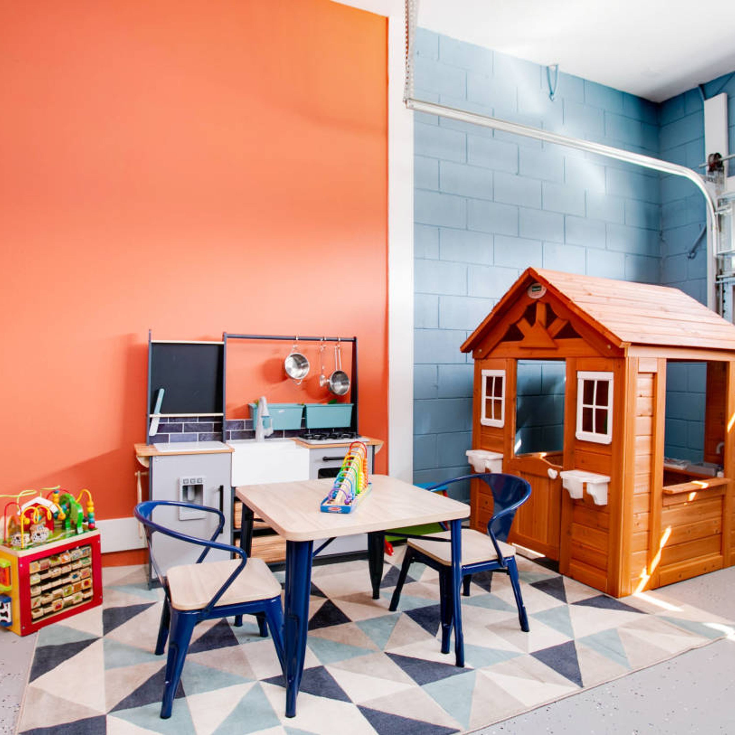 Ein Spielzimmer für Kinder mit einem Spielhäuschen, einem Tisch mit Stühlen und einer bunten Spielecke.
