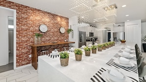A modern kitchen with a brick wall, stainless steel appliances, and a long dining table set for six. - Unique Masterpiece15 Suites Sleeps 30 Son101 (Kissimmee)