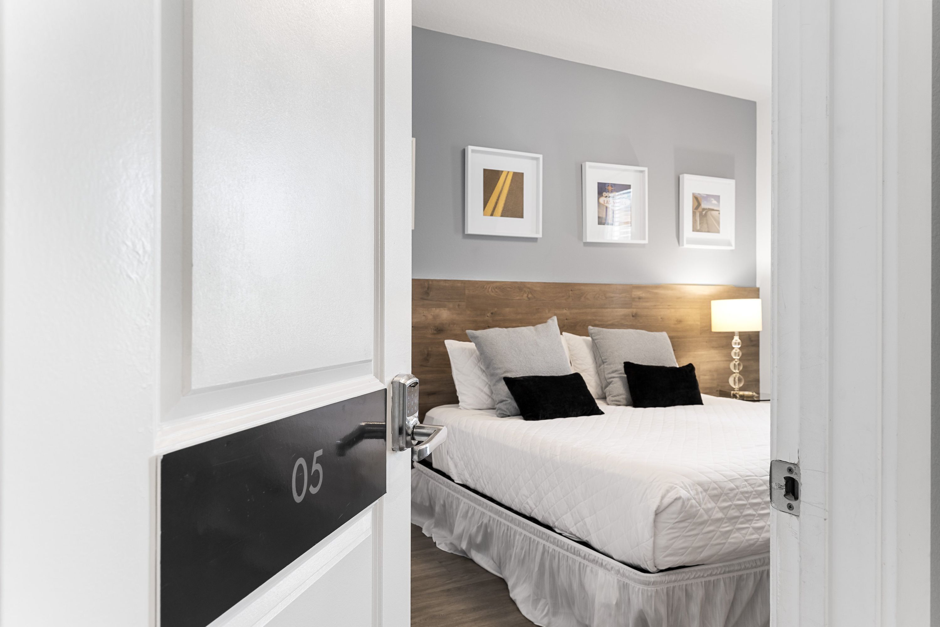 A hotel room with a bed, a wooden headboard, a nightstand, and a wall-mounted lamp.