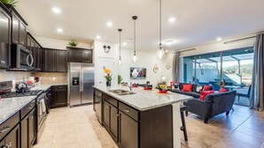Une cuisine moderne avec des meubles de couleur sombre, un îlot central, des appareils électroménagers en acier inoxydable et des luminaires suspendus.