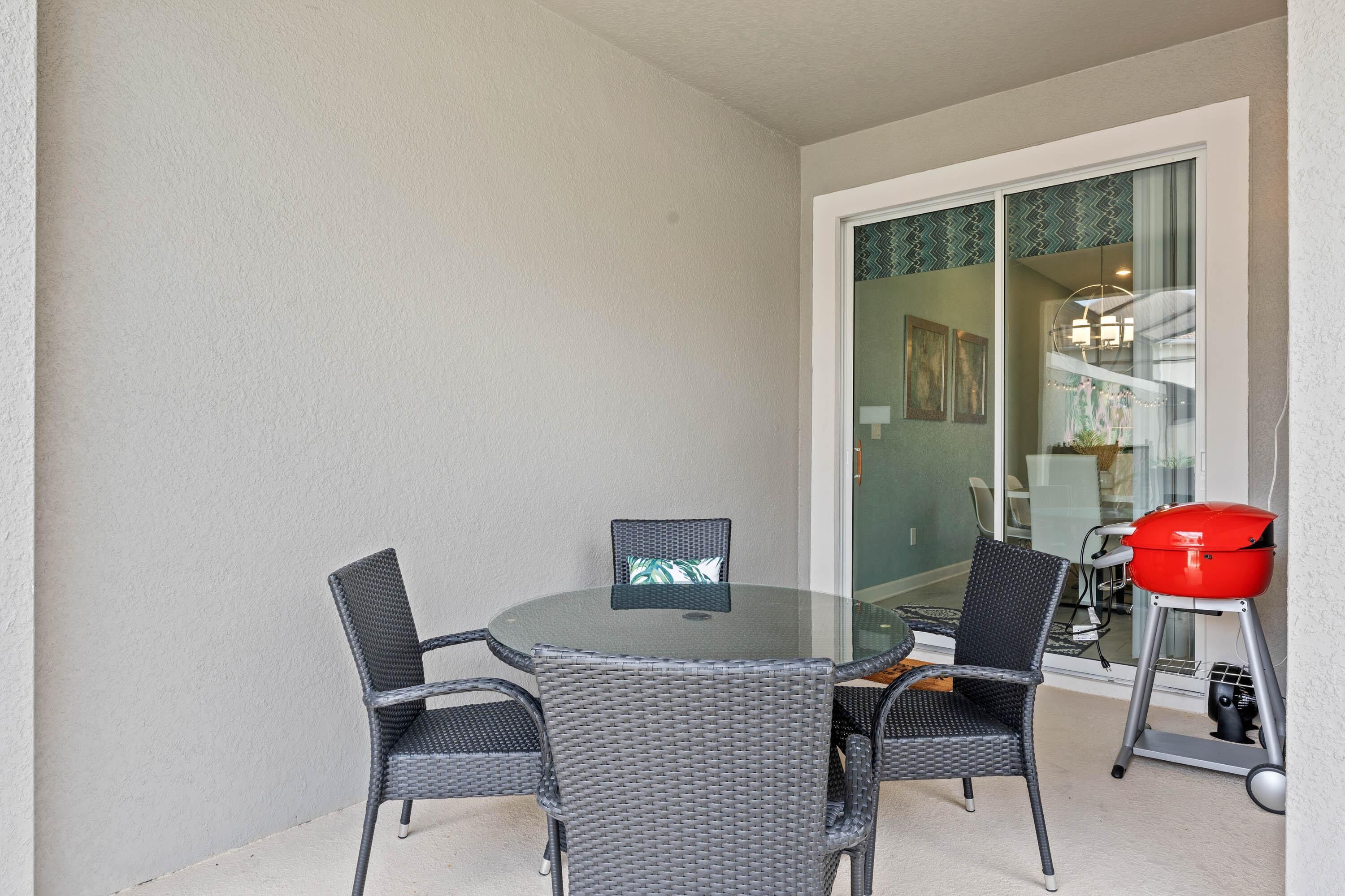 A round table with four chairs, a red grill, and a sliding glass door leading to a balcony.