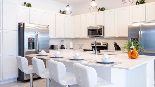 A modern kitchen with white cabinetry, stainless steel appliances, and a central island with bar stools.