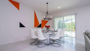A modern dining area with a marble floor, white chairs, a glass table, and a chandelier.