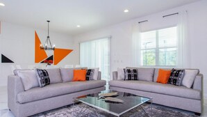 A modern living room with two grey sofas, a glass coffee table, and a geometric wall decoration.