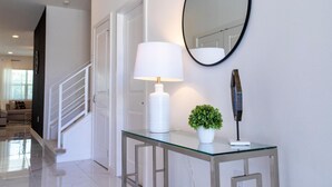 A modern hallway with a glass console table, a white lamp, a small potted plant, and a round mirror on the wall.