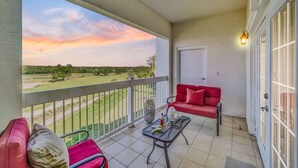 Un balcon avec un canapé rouge, une petite table et une vue sur un terrain de golf.