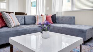 A modern living room with a grey sectional sofa, a white coffee table, and a vase with purple flowers. - Comfy House at Compass Bay Cb102 (Kissimmee)
