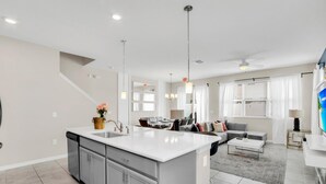 A modern kitchen with a large island, a dining area with a sofa, and a living room with a TV. - Comfy House at Compass Bay Cb102 (Kissimmee)
