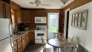 Una cocina compacta con armarios de madera, un refrigerador blanco, un microondas, un horno y una mesa de comedor con sillas.