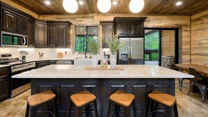 A modern kitchen with dark wood cabinets, stainless steel appliances, and a large island with bar stools. - Stars & Streams - Ev Outlet, Pool Table,Shuffleboard, Hot Tub, Arcade Console (Broken Bow)