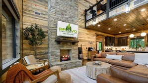 A cabin interior with a stone fireplace, wooden walls, a dining area, and a kitchen. - Stars & Streams - Ev Outlet, Pool Table,Shuffleboard, Hot Tub, Arcade Console (Broken Bow)