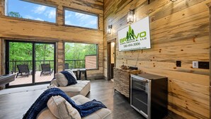 A cabin with a wooden interior, a large window, and a sign for BravO Cabin Rentals, LLC. - Stars & Streams - Ev Outlet, Pool Table,Shuffleboard, Hot Tub, Arcade Console (Broken Bow)