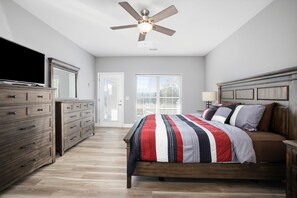 Quarto com cama, cómoda de madeira, ventoinha de teto e televisão.