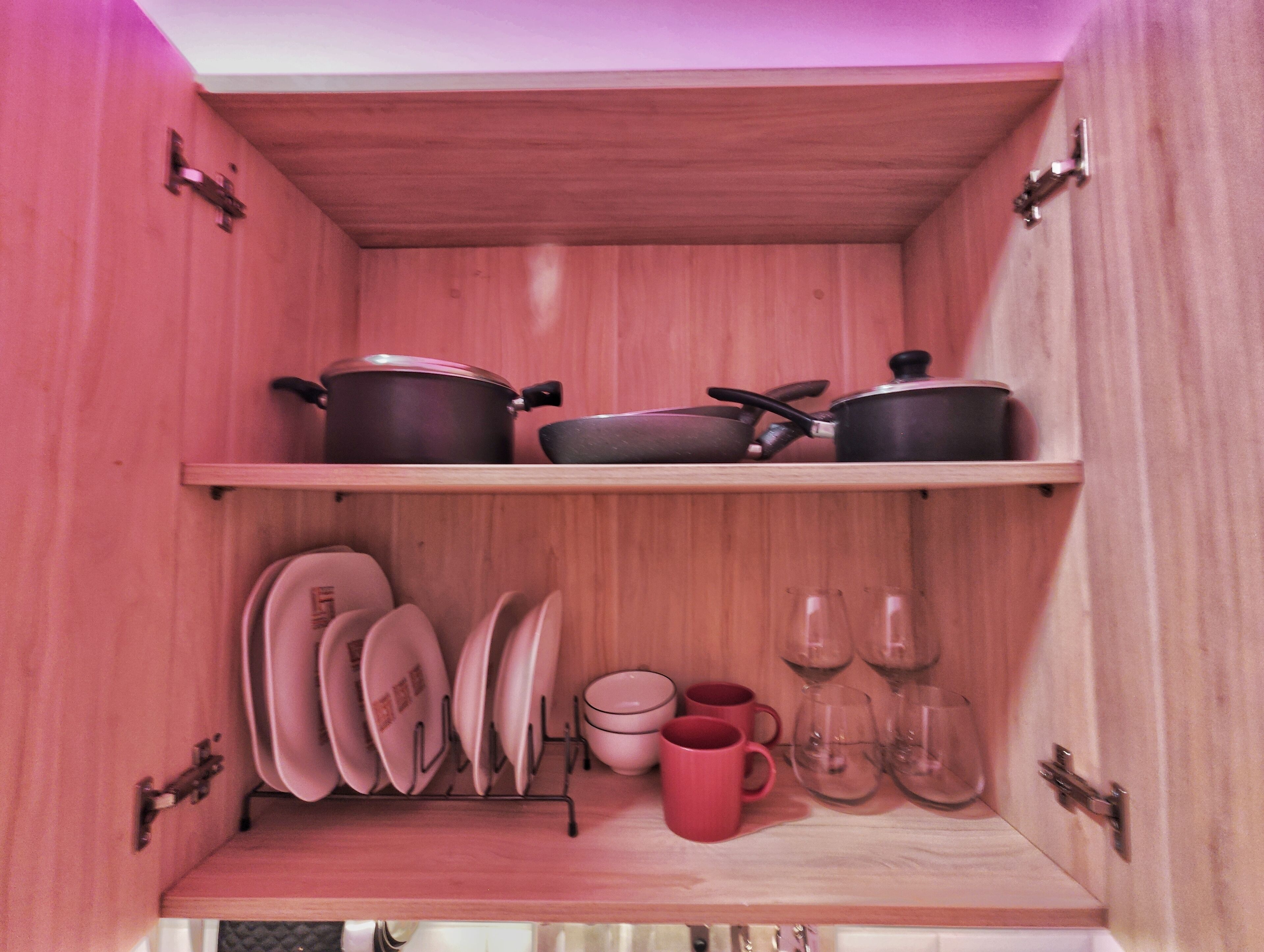A wooden cabinet with shelves holding pots, pans, plates, cups, and glasses.