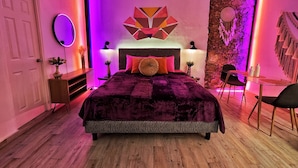 Quarto moderno com uma cama grande, um espelho redondo e uma obra de arte geométrica na parede.