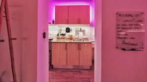 Corredor estreito que leva a uma cozinha com iluminação rosa, armários de madeira e um letreiro de boas-vindas.