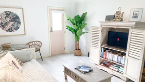 Una sala de estar con un sofá, una mesa de centro, una estantería, un televisor y una planta en maceta.