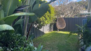 Un jardín con hojas verdes grandes, una valla de madera y una silla de mimbre.