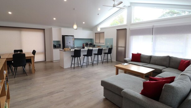 A modern living room with a grey sofa, a wooden coffee table, and a dining area with a wooden table and chairs.