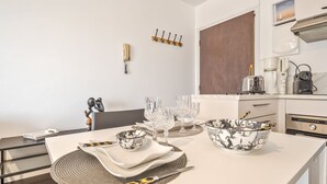 A modern kitchen with white countertops, a dining table set with glassware and plates, a coffee machine, and a microwave. - Le Manon by Interhome (Dinard)