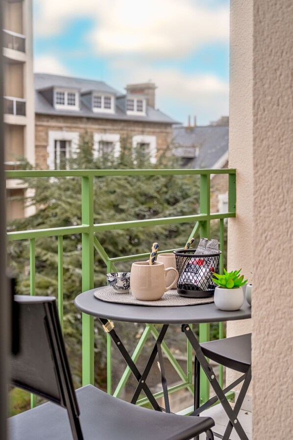 A balcony with a small table, two chairs, a potted plant, and a coffee maker.