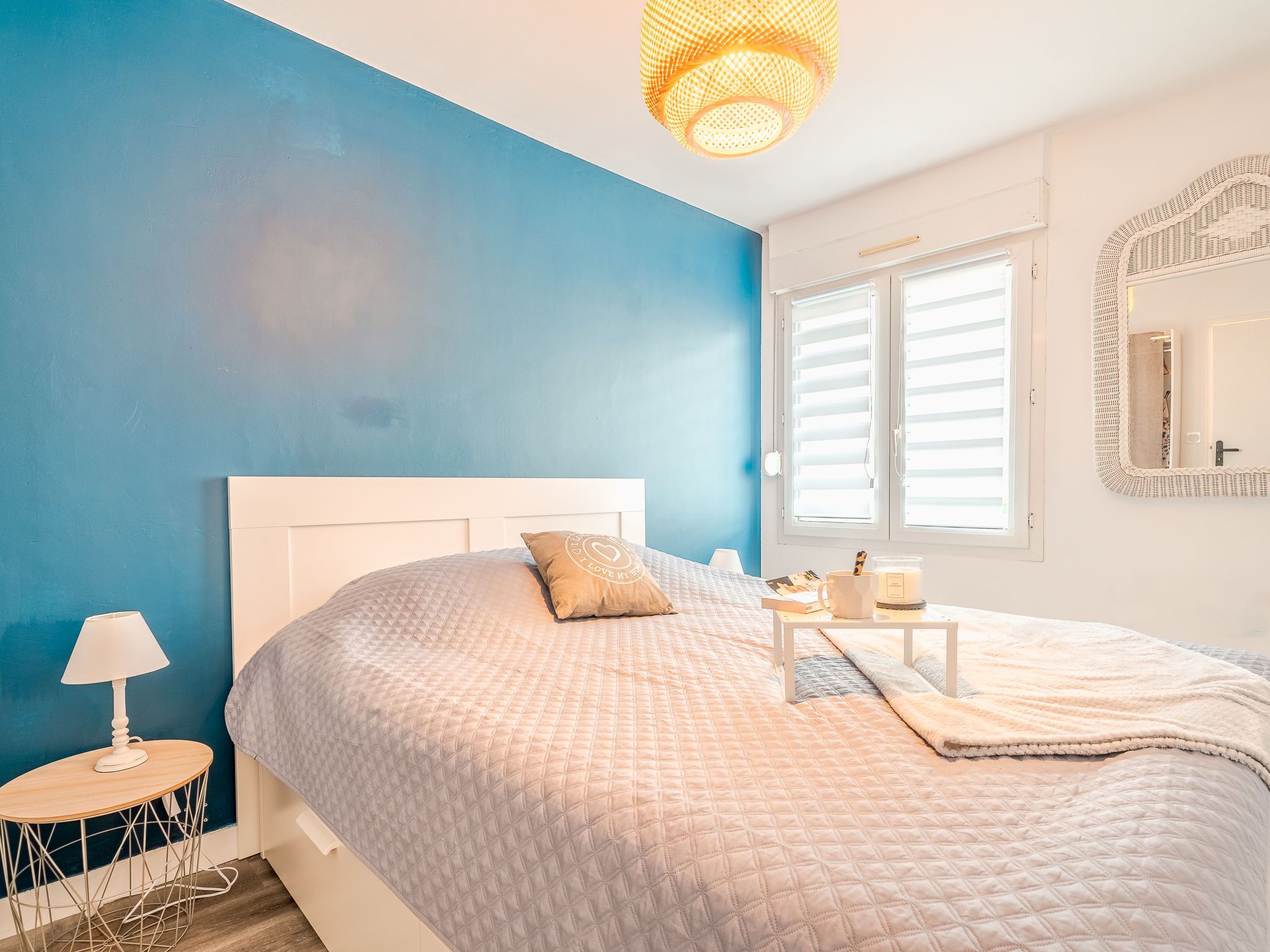 Une chambre à coucher avec un lit, une table de chevet, une lampe et une fenêtre avec des stores.