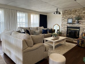 En stue med en beige sofa, et sofabord, en pejs og en stenvæg.