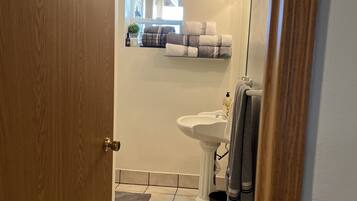 Un baño con puerta de madera, un lavamanos blanco, un espejo y un perchero para toallas.