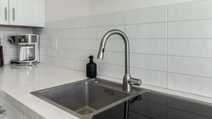 A kitchen with a stainless steel sink, a coffee maker, and a black soap dispenser. - Hang Ten at the Studio! Vibe in This Groovy Avila Beach Studio Condo! (Avila Beach)