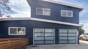A modern two-story house with a dark blue exterior, two garage doors, and a wooden fence. - Hang Ten at the Studio! Vibe in This Groovy Avila Beach Studio Condo! (Avila Beach)