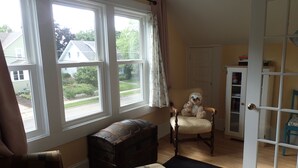 A room with a large window, a wooden chest, a chair, and a door with a glass panel.
