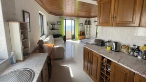 A modern kitchen with wooden cabinets, a marble countertop, and a dining area with a sofa.