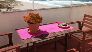 A wooden table with a potted plant and a bowl of stones on a balcony overlooking the ocean.