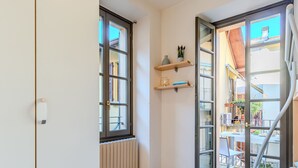 A room with a radiator, a white wardrobe, a window with a view, and a door leading to an outdoor area.