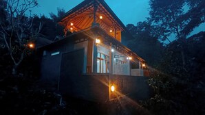 Un edificio de dos pisos con techo inclinado, múltiples ventanas e iluminación exterior.