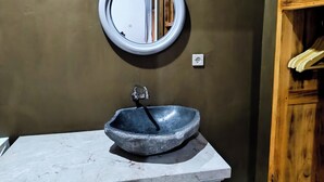 Un baño con un espejo redondo, un lavamanos de piedra y un estante de madera.