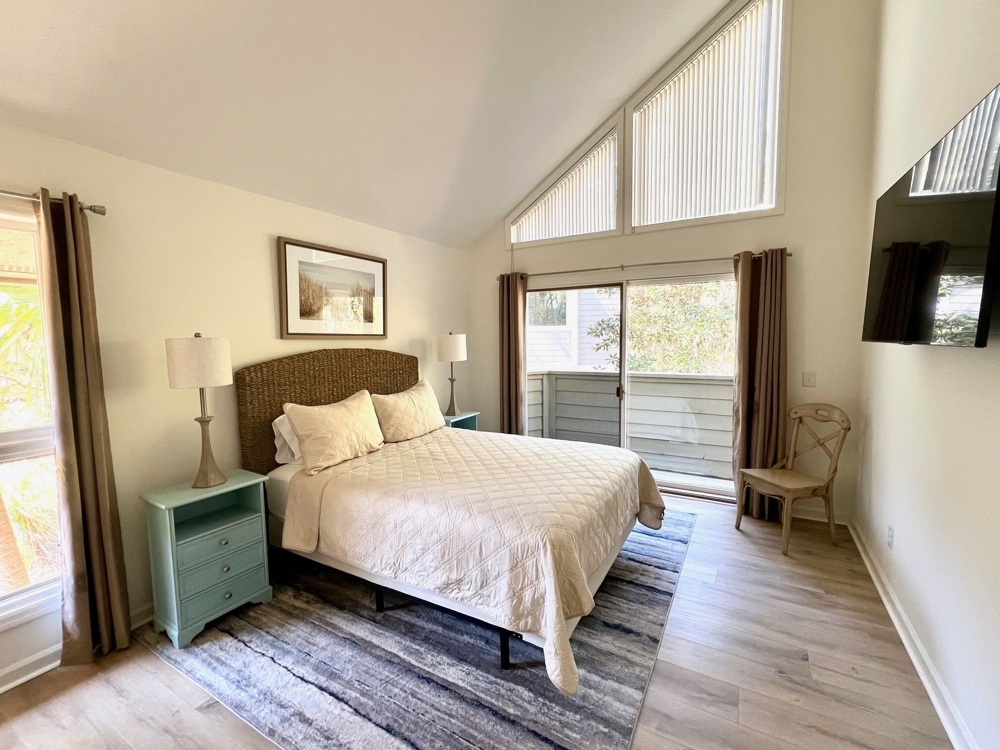A bedroom with a bed, nightstands, a chair, a picture on the wall, and a window with curtains.