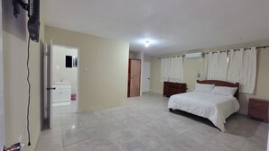 A bedroom with a bed, a nightstand, a dresser, and a door leading to another room.