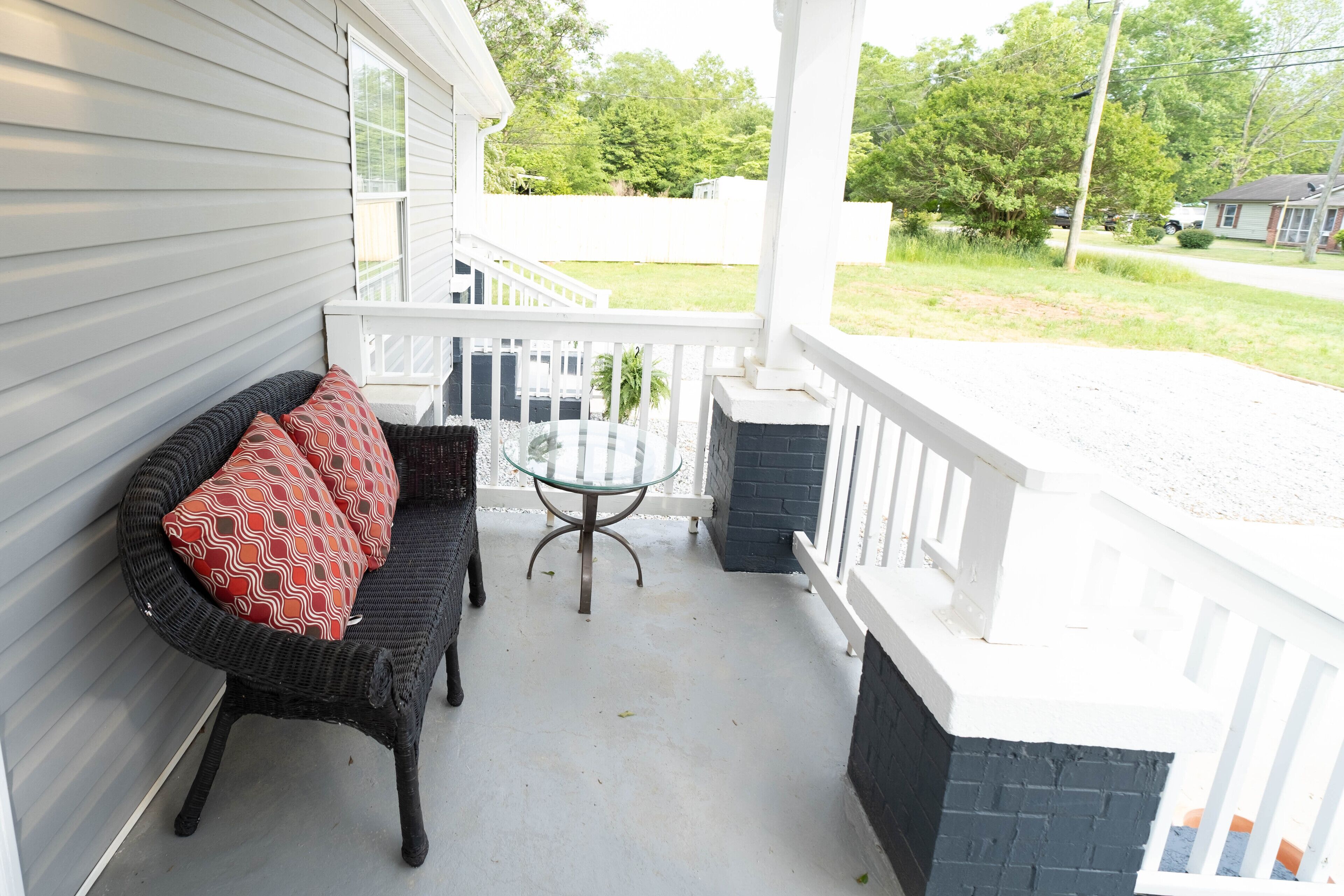 A covered porch with a wicker sofa and a glass table.