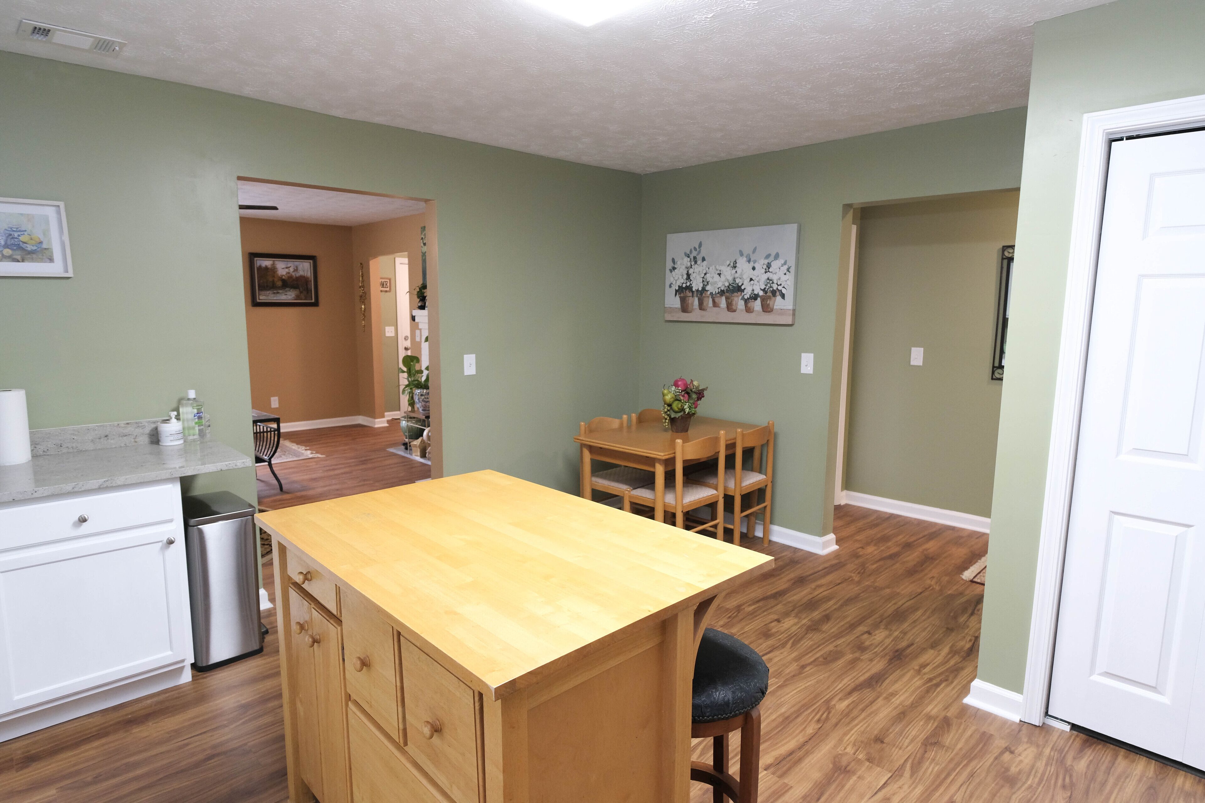 A kitchen with wooden cabinets, a countertop, and a dining area with a table and chairs.