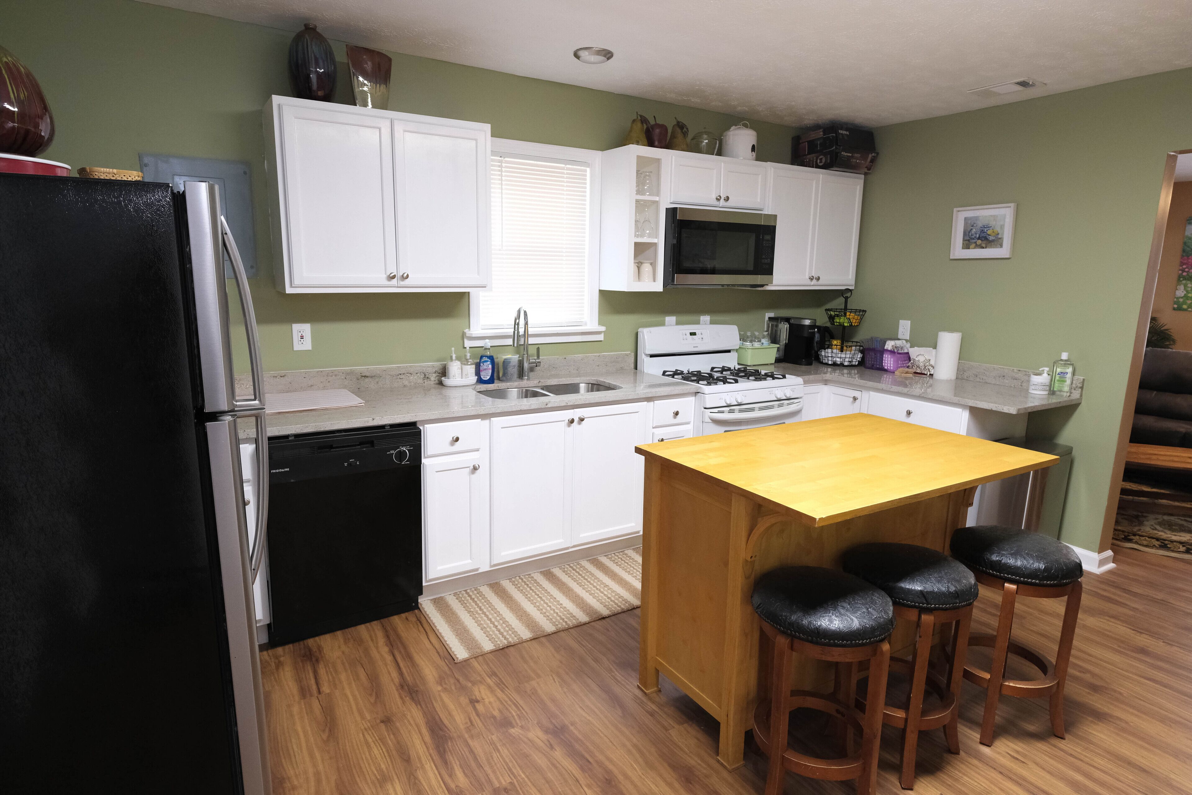 A kitchen with white cabinets, a black refrigerator, a wooden island with stools, a microwave, and a stove.