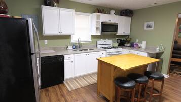 A kitchen with white cabinets, a black refrigerator, a wooden island with stools, a microwave, and a stove.