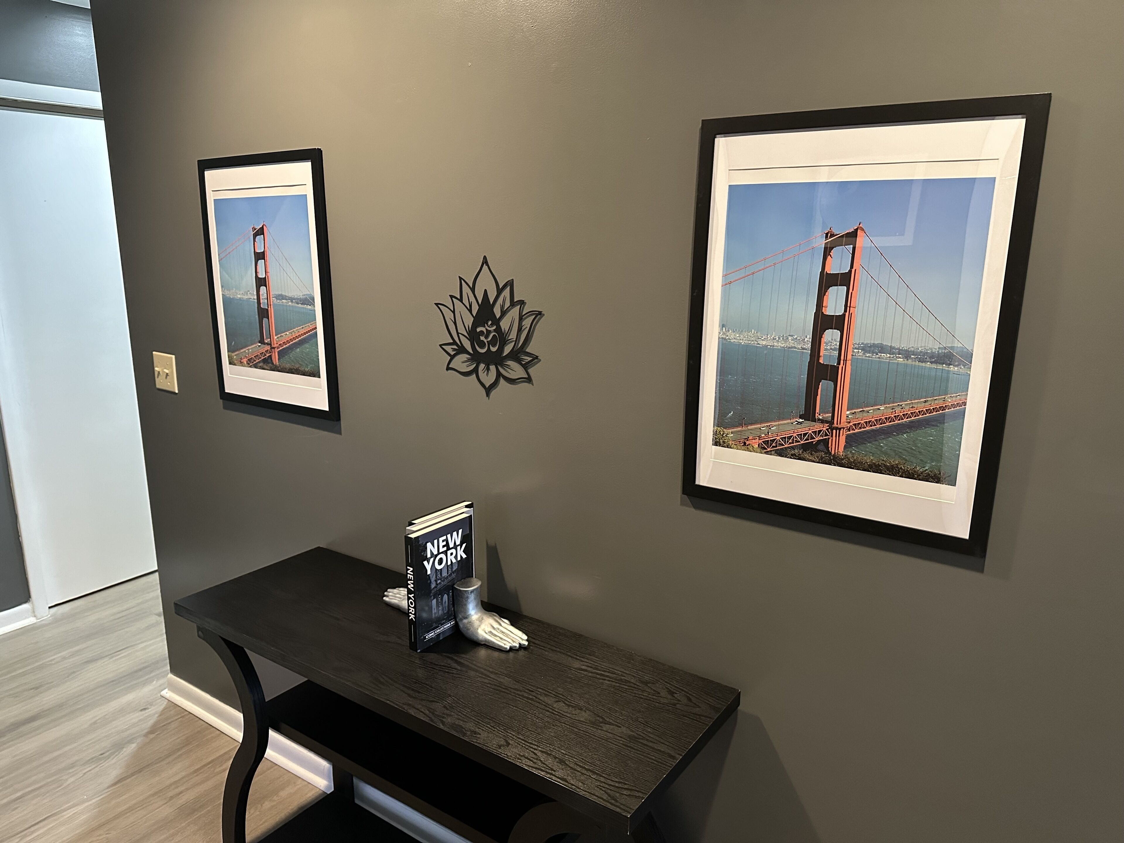 Ein Zimmer mit zwei gerahmten Bildern der Golden Gate Bridge, einem kleinen Tisch mit einem Buch mit dem Titel 'New York' und einem dekorativen Wandkunstwerk.