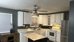 A modern kitchen with white cabinets, a wooden countertop, a black island, a ceiling fan, and a stainless steel refrigerator. - Retreat to my Beautiful Contemporary Home in the Mountain State (Morgantown)