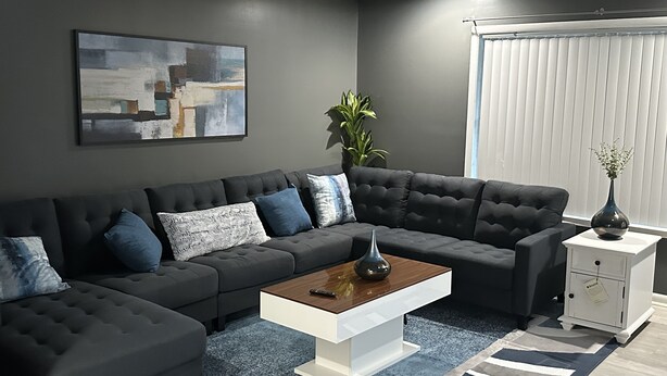 A modern living room with a sectional sofa, a coffee table, a side table, and a potted plant. - Retreat to my Beautiful Contemporary Home in the Mountain State (Morgantown)