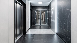 Un pasillo moderno con piso de mármol, puertas de ascensor metálicas y una señal con números en la pared.
